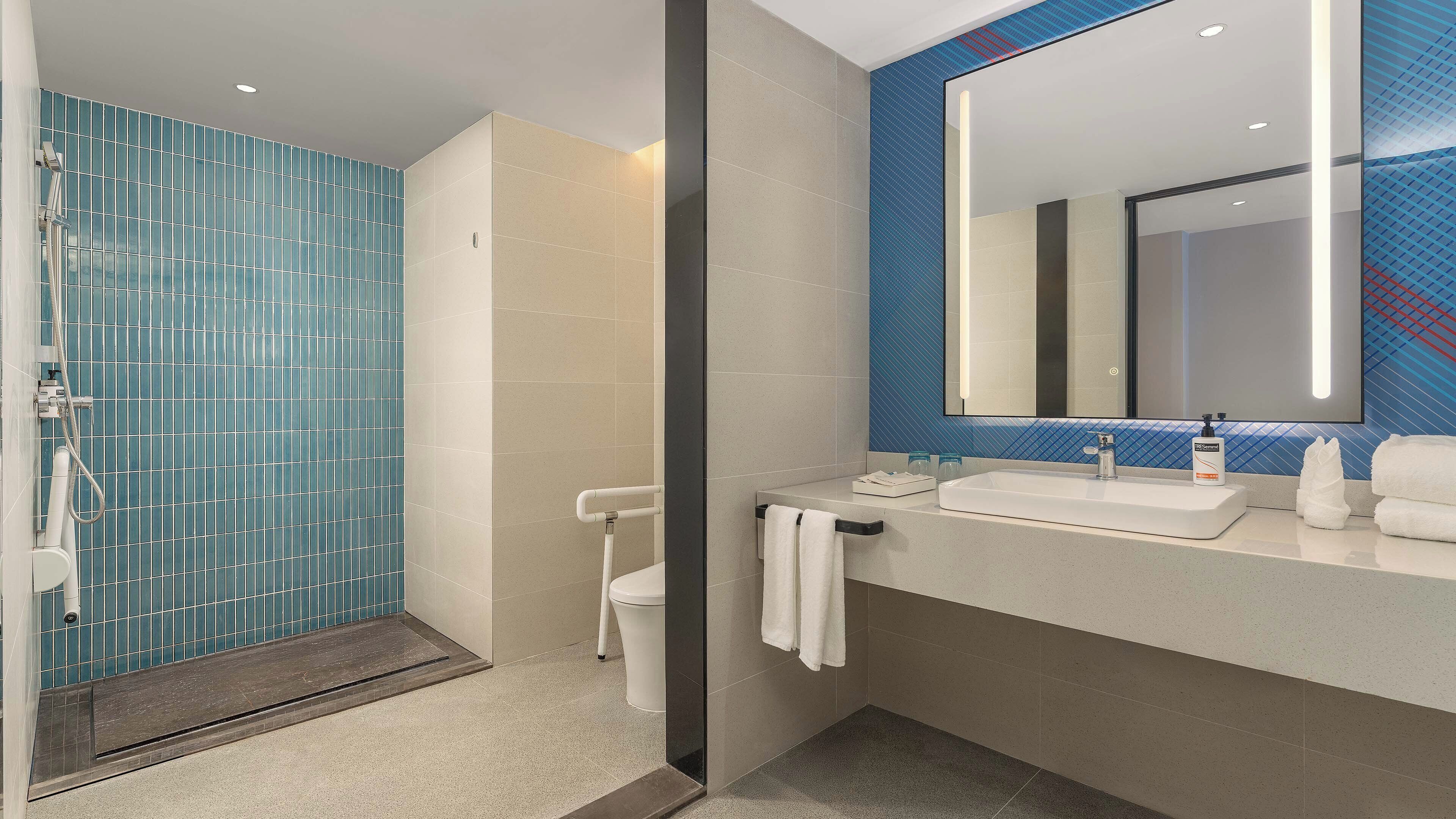 Une salle de bain moderne avec une douche à parois de verre, des toilettes, un lavabo avec un miroir et un porte-serviettes.