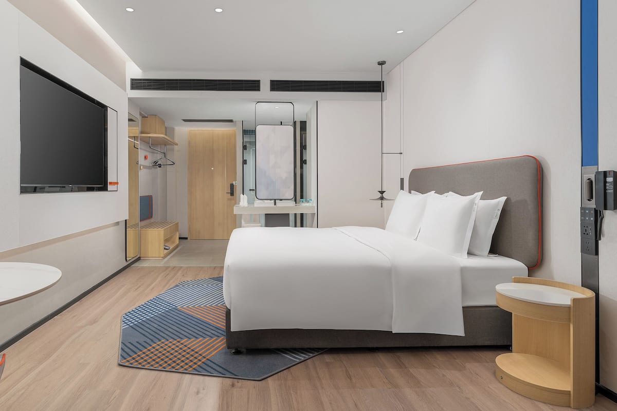 A modern hotel room with a bed, a desk, a TV, and a bathroom.