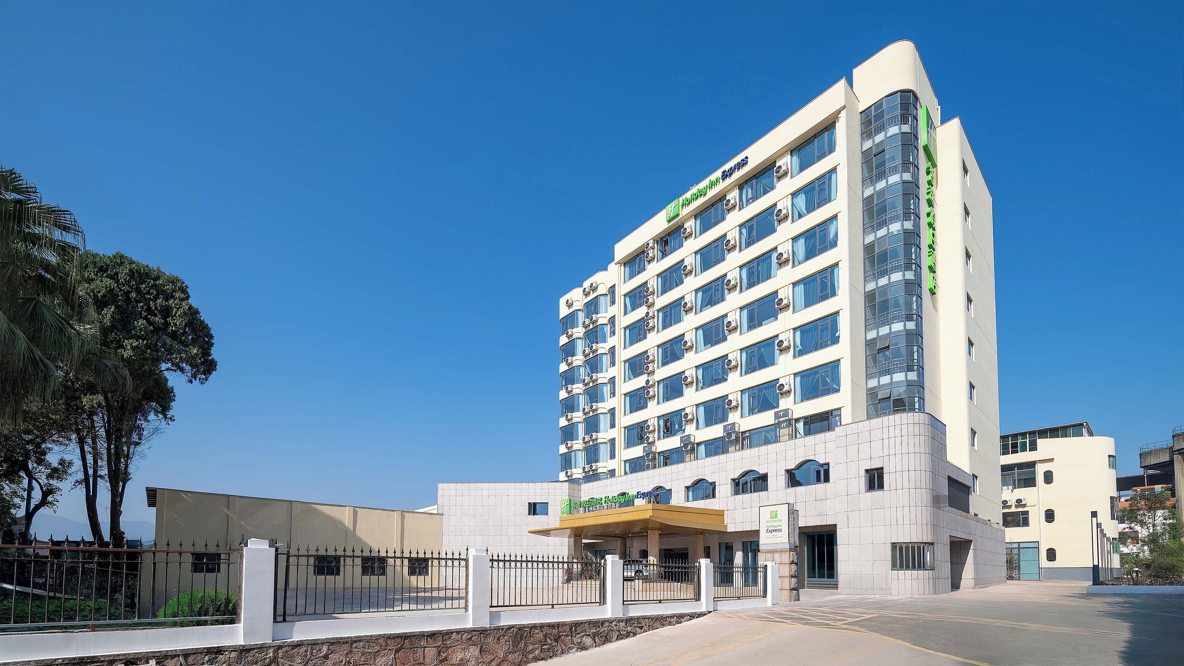 Un hotel moderno con un llamativo letrero verde, varios equipos de aire acondicionado y una entrada con portón.