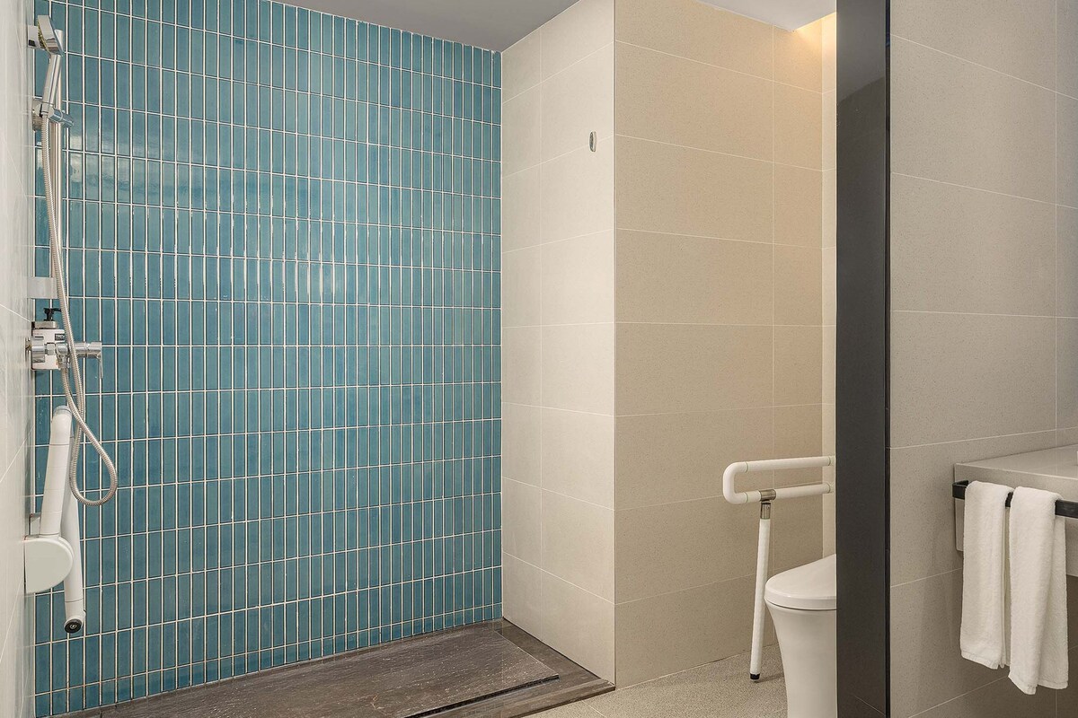 A bathroom with a blue-tiled shower enclosure, a white toilet, and a sink with a mirror above it.
