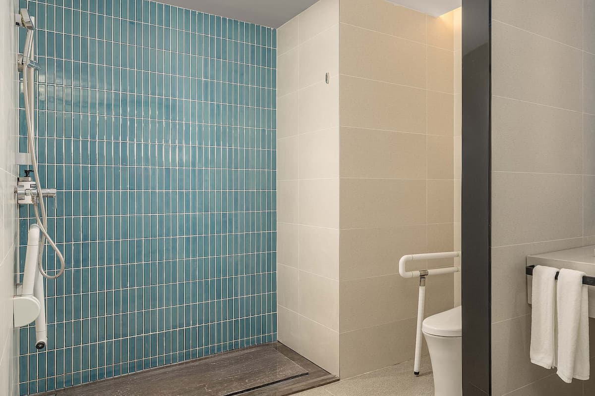 A bathroom with a blue-tiled shower enclosure, a white toilet, and a sink with a mirror above it.