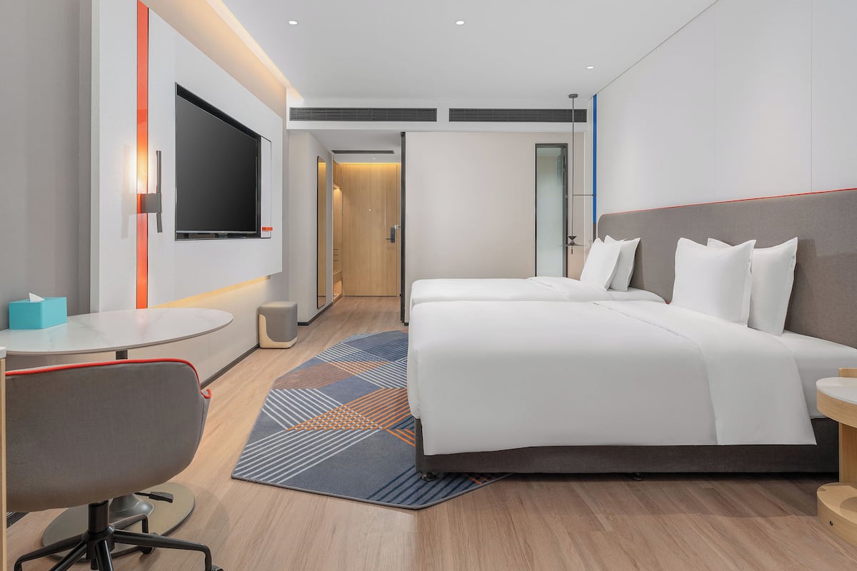 A modern hotel room with a bed, desk, chair, and a TV mounted on the wall.