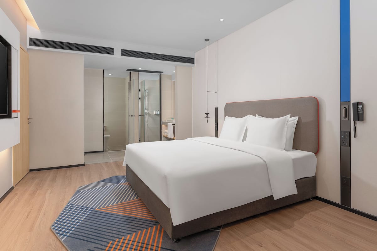 A modern hotel room with a large bed, a flat-screen TV, a shower, and a bathroom with a glass door.