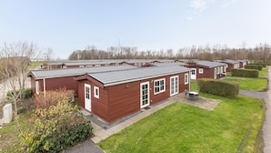 A row of red wooden mobile homes with grey roofs, arranged in a neat row with green lawns and trimmed bushes in front. - Cozy home in Wagenborgen with WiFi (Wagenborgen)