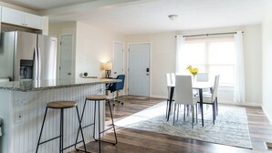 Eine moderne Küche mit Einbaukühlschrank, Barhocker und einem Essbereich mit Tisch und Stühlen.