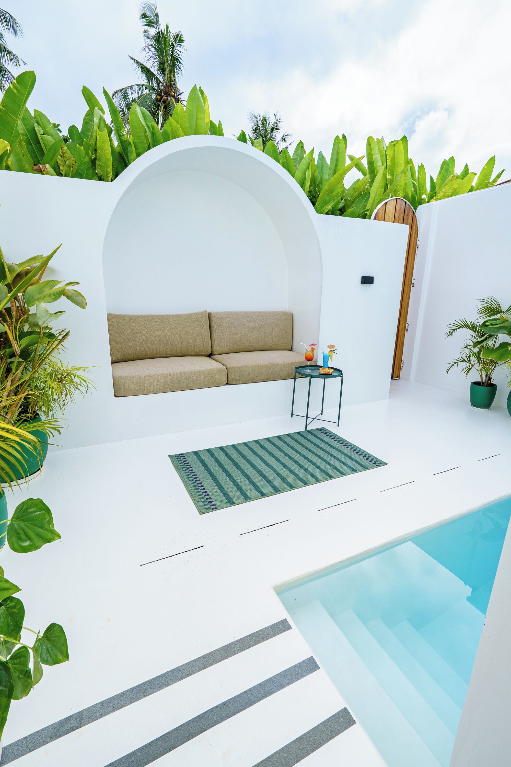 A modern outdoor living area with a pool, a sofa, and potted plants.