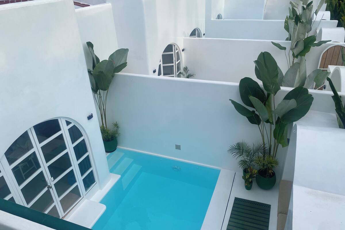 A pool area with a clear blue pool, surrounded by white walls and potted plants.