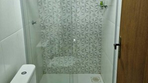 A small, enclosed shower area with a geometric tile pattern, a toilet, and a towel on the floor.