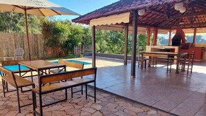 An outdoor patio with stone flooring, a pool, and a covered barbecue area.