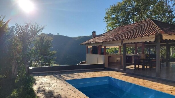 A swimming pool with stone tiles, a covered outdoor seating area, and a view of a mountainous landscape.