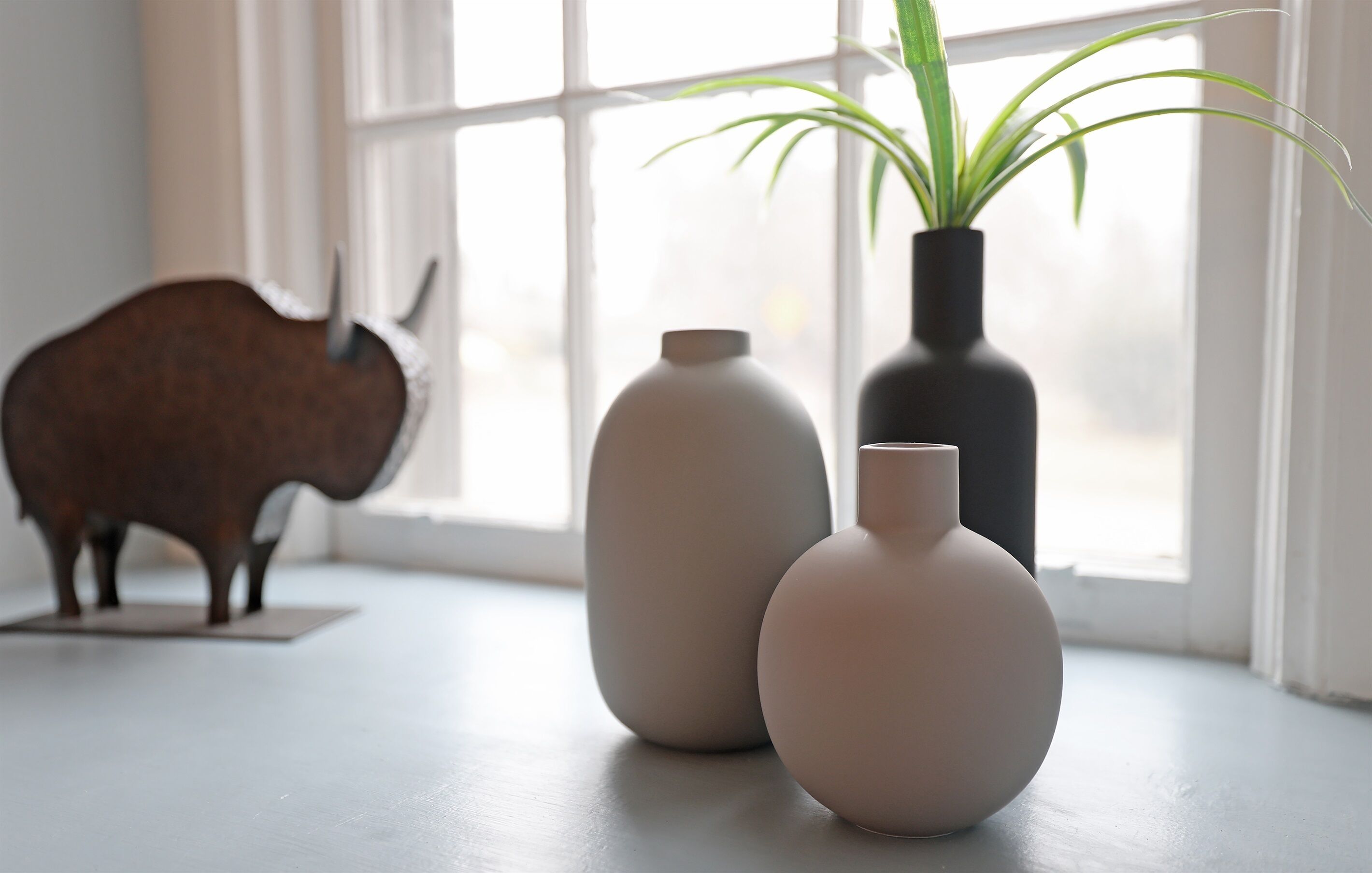 Drie vazen op een vensterbank, met een stierbeeldje en een plant.