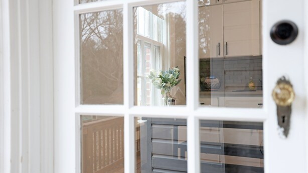 A white door with a glass panel, a keyhole, and a view of a kitchen with cabinets and a countertop.