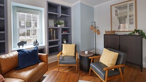 A living room with a brown leather sofa, two grey armchairs, a wooden coffee table, and a bookshelf with decorative items.