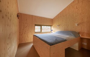 Cozy retreat with a slanted ceiling and wooden paneling, featuring a comfortable bed and natural light.
