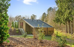 Situated in a wooded area, this single-story house features a covered porch and a prominent front entrance with a glass door.