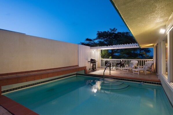 Ein Schwimmbad mit überdachter Terrasse, Grill und Sitzgelegenheiten im Freien.