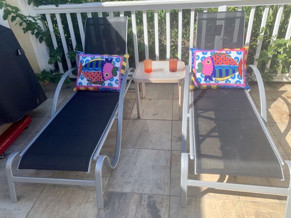 Two sun loungers with mesh screens and colorful cushions, a small table with drinks, and a barbecue grill. - Luxury Private Pool Villa. Grill. Generator@Sapphire (Red Hook)