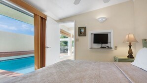 A hotel room with a bed, a TV mounted on the wall, a lamp, and a view of a swimming pool.