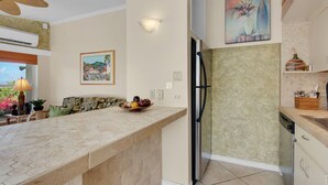 A kitchen with a central island, a refrigerator, and a dining area with a sofa and a table.