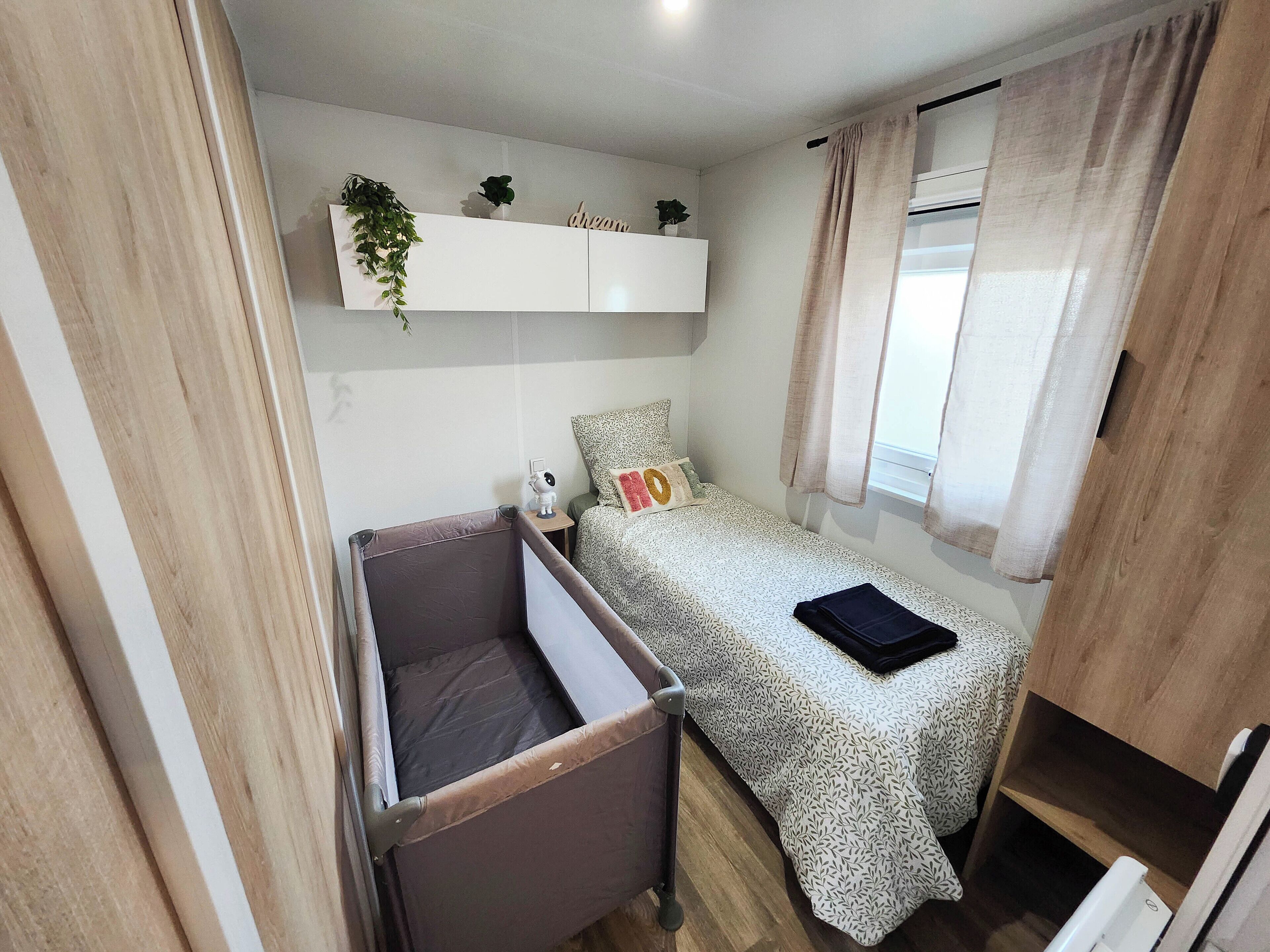 A compact bedroom with a bed, a small bedside table, a hanging plant, and a window with curtains.