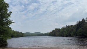 A natural landscape with a lake, forested hills, and a sandy beach.