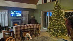 A cozy living room with a fireplace, a television, a Christmas tree, and a dining area.