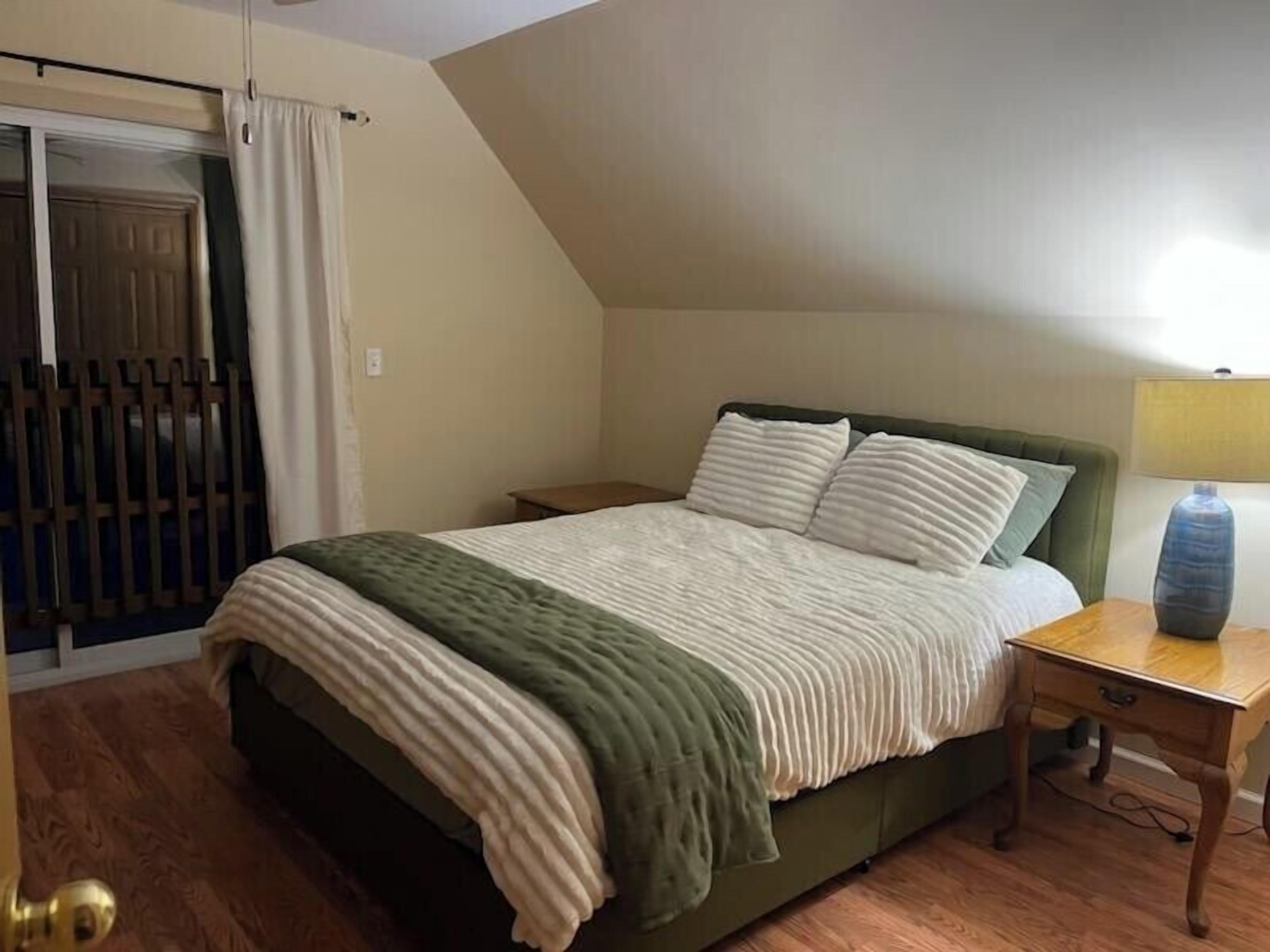 A bedroom with a bed, a nightstand, a lamp, and a window with curtains.