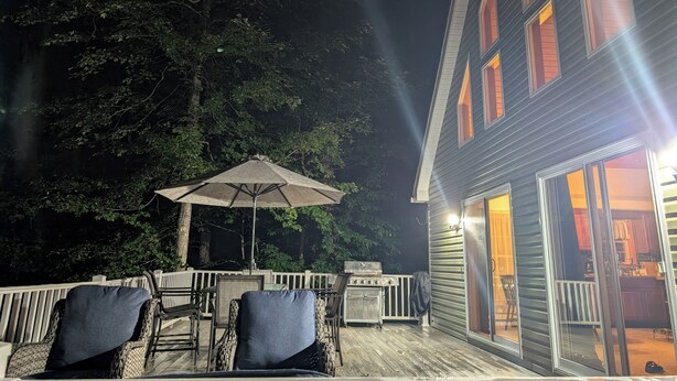 An outdoor patio with wicker furniture and a grill, surrounded by trees.