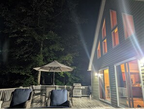 Un patio al aire libre con mobiliario de mimbre y una parrilla, rodeado de árboles.