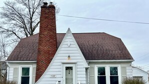 A single-story house with a brick chimney, white siding, and a front porch.