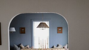 A dining area with a wooden table, chairs, and a chandelier. There is a window with a view of the outside.