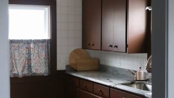 A kitchen with dark brown cabinets, a marble countertop, a window with a patterned curtain, and a woven ceiling light fixture.