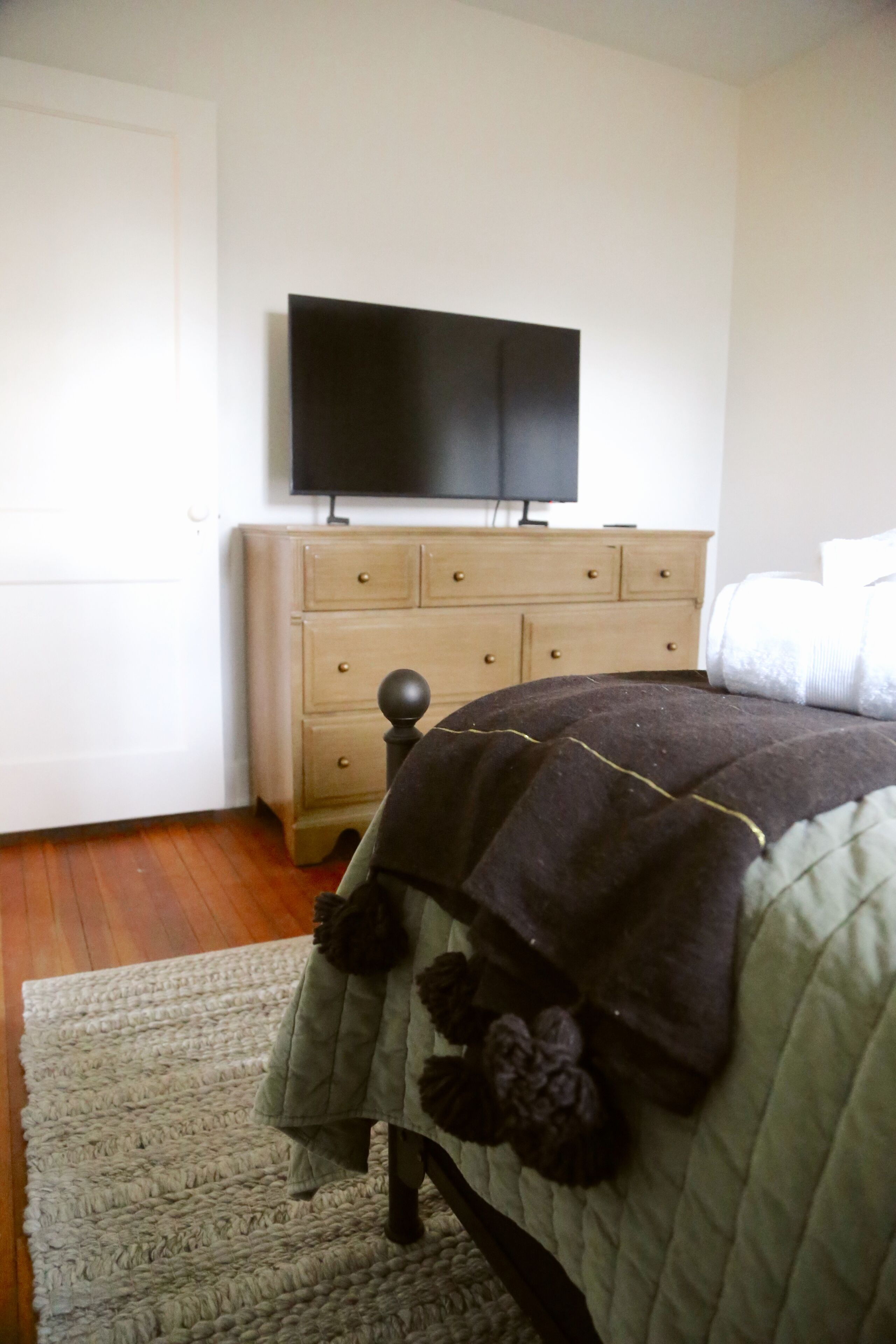 A bedroom with a bed, a dresser, and a television on the wall.