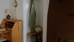 A room with a white armchair, a small round table, a wooden desk with drawers, a green towel hanging, a clock, and a fireplace.