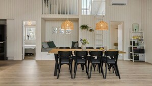 Un grand espace à manger avec une table en bois et des chaises noires, un canapé avec des coussins et deux lampes suspendues en osier.