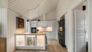Une cuisine moderne avec des meubles blancs, un îlot central en bois doté de placards à portes vitrées et un réfrigérateur noir.