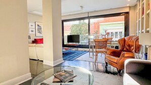 A modern living room with a glass coffee table, leather sofa, and a view of the outside.