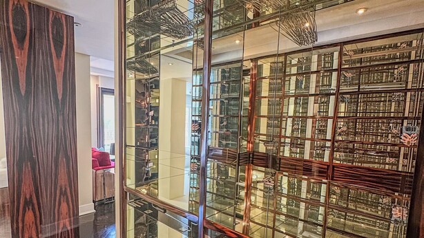 A modern interior with a large glass display case filled with books and a wooden panel with a geometric pattern.