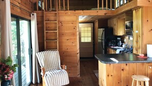 Interno di una baita in legno con cucina, zona pranzo e angolo salotto accogliente, con una sedia e un tavolo.