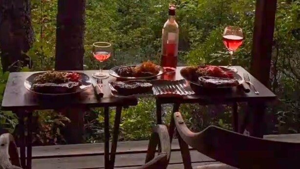 Un tavolo da pranzo all'aperto con una bottiglia e dei bicchieri.