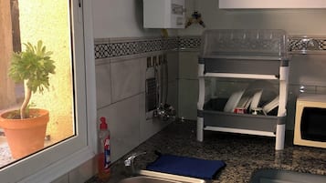 A kitchen with granite countertops, a stainless steel sink with a red basin, a microwave, a dish rack, and a potted plant by the window.