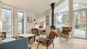 Ein gemütliches Blockhaus-Interieur mit Holzwänden, einem großen Fenster, einem Kamin und einer komfortablen Sitzecke.