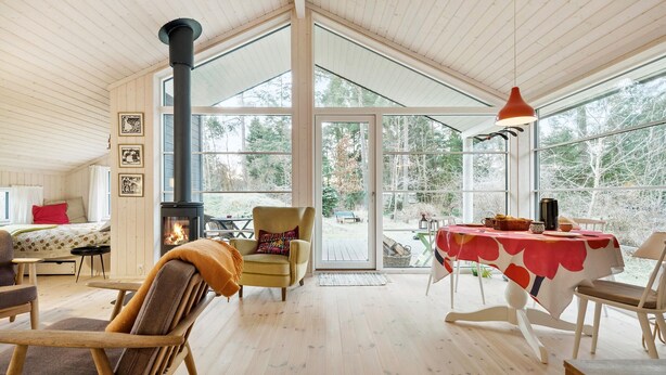 Ein gemütliches Zimmer mit Holzvertäfelung, einem Kamin und großen Fenstern mit Blick ins Freie.
