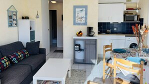 Un espacio habitable compacto con sofá, mesa de comedor, zona de cocina con microondas y lavadora, además de un pequeño vestíbulo.