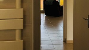 Ein Zimmer mit Meerblick durch große Fenster, ein schwarzer Stuhl und ein Fliesenboden.