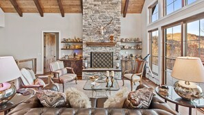 A spacious living room with a stone fireplace, leather furniture, and a large window offering a view of the outdoors. - Sunbird Cabin at MontEagle - new, EV charger, hot tub, King rooms (Banner Elk)