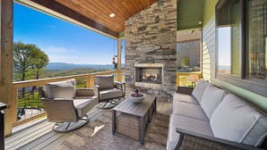 A wooden deck with outdoor furniture, a stone fireplace, and a scenic view. - Sunbird Cabin at MontEagle - new, EV charger, hot tub, King rooms (Banner Elk)