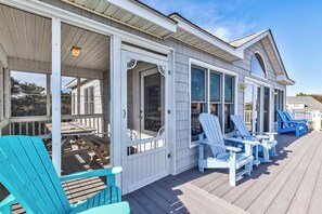 A covered deck with blue Adirondack chairs and a white building with large windows. - True North | 375 ft to the beach (Duck)