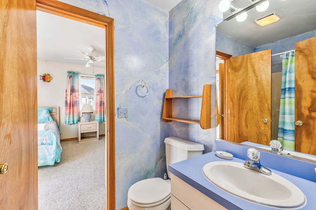 A bathroom with a blue-tinted wall, a white sink, and a wooden vanity.