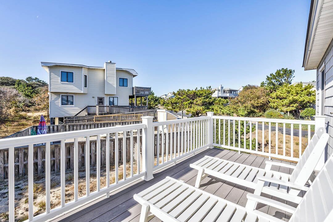 A two-story house with a deck, white railings, and a view of the surrounding landscape.